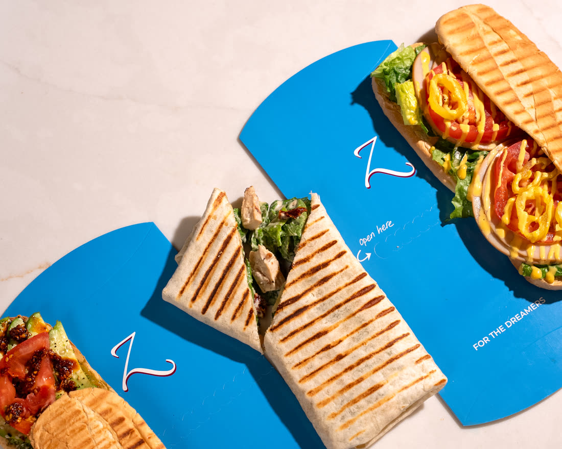 Three Z Cafe paninis and a wrap laid out on blue for-the-dreamers sleeves